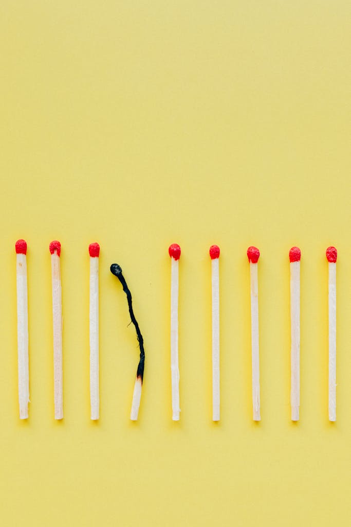 A line of matchsticks with one burned out symbolizes burnout and exhaustion against a yellow background.