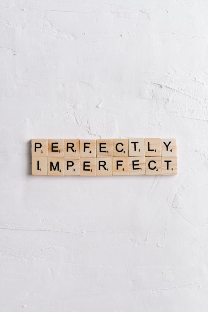 Scrabble tiles on white surface spell 'Perfectly Imperfect' with ample copy space.